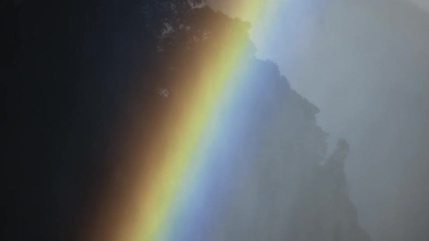 View of a rainbow with trees in the background during a drizzle
