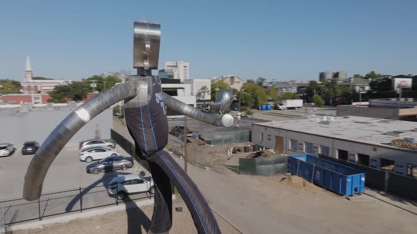 Large sculpture of guitar headed basketball player towers over street with skyline in the background