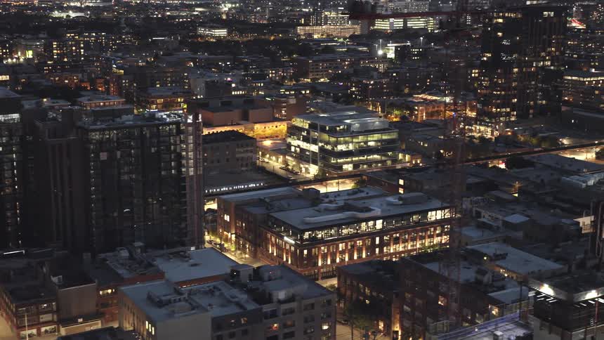 Trains travel along railway through brightly lit cityscape at night