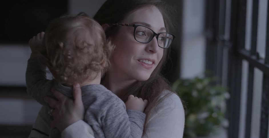 Woman holds a baby while looking out a window