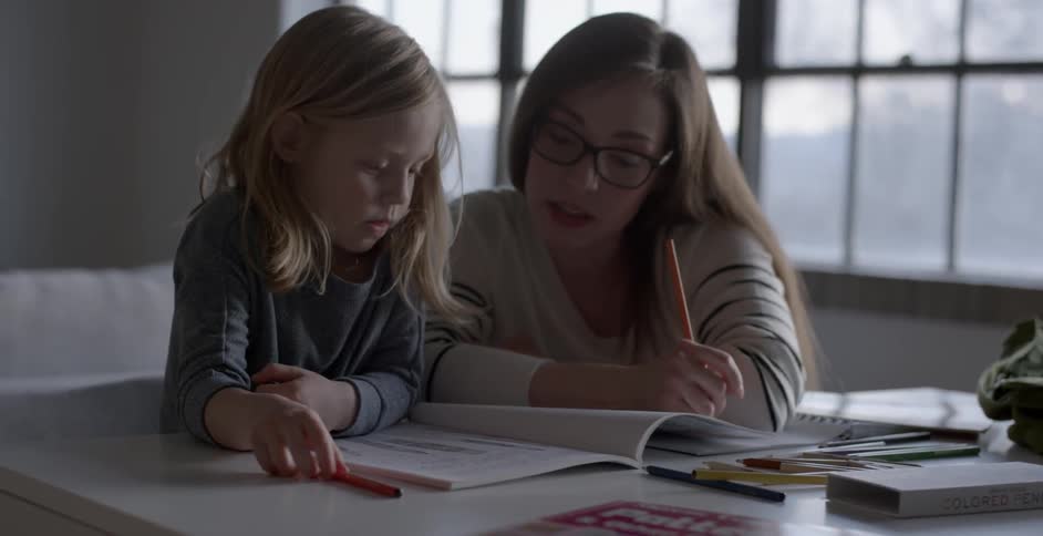 A mother and daughter color in a coloring book at home