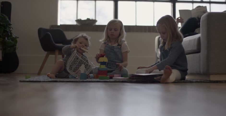 Two girls and a baby play with toys on a rug on the floor