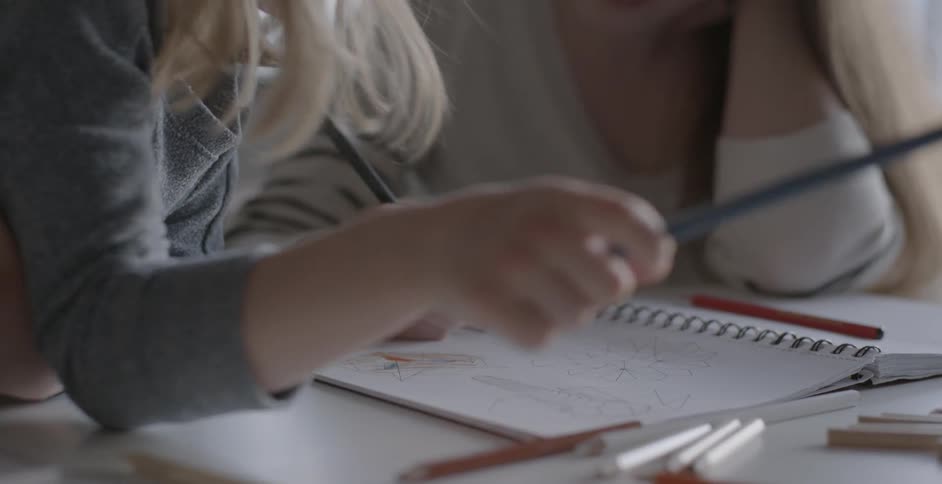A girl draws on a notebook with a pen