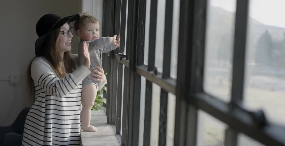 A baby and woman wave out of a window