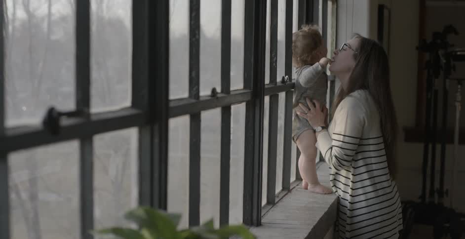 Woman holds a baby on a window sill