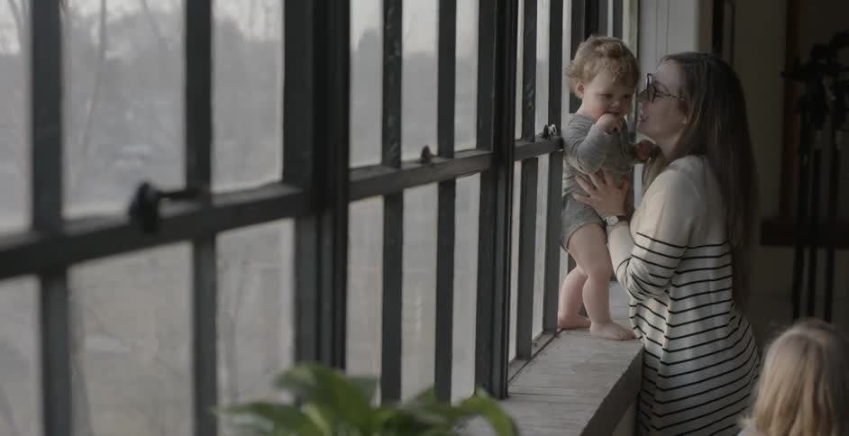 A woman kisses a baby by the window