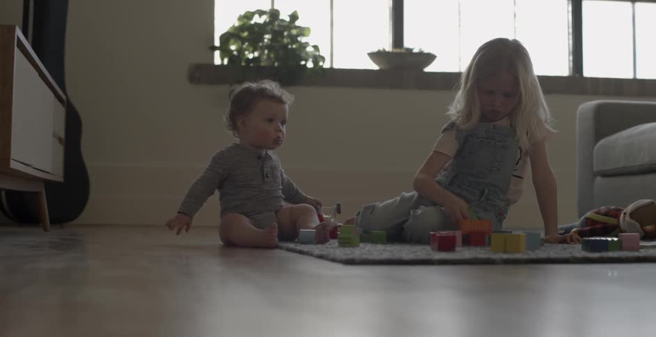 Two children play on a mat near a window