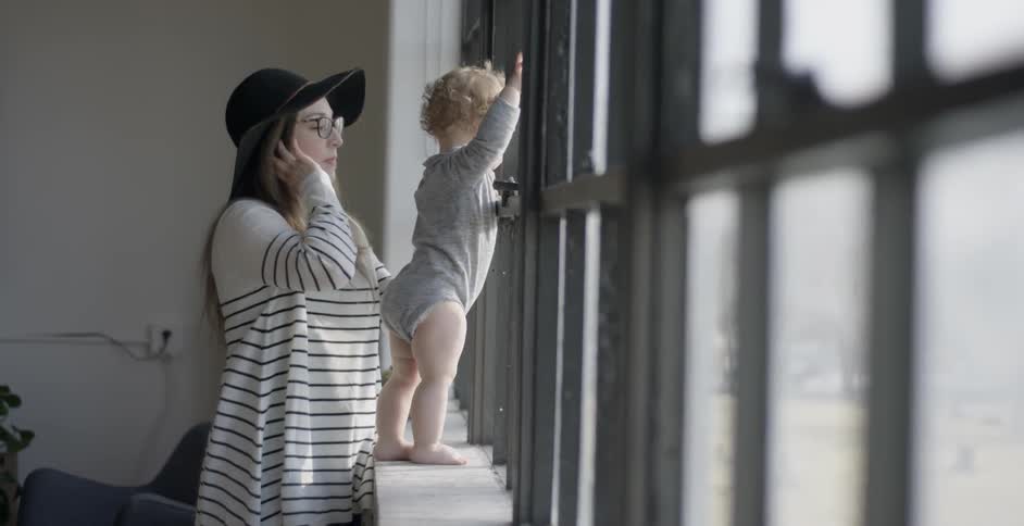 A woman watches a baby who is leaning against a window