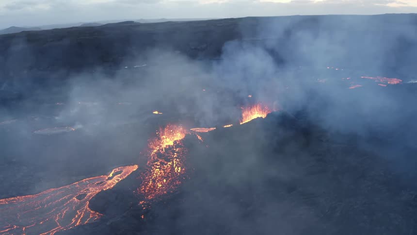 Molten hot lava glows as it splashes from an erupting volcano and smoke fills the air as lava flows
