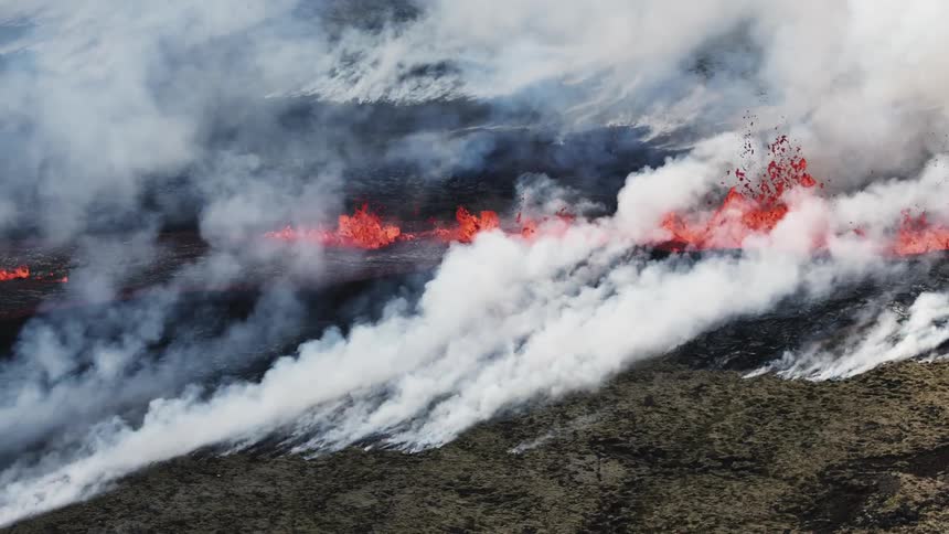Molten hot lava splashes as it flows from an erupting volcano and smoke fills the air