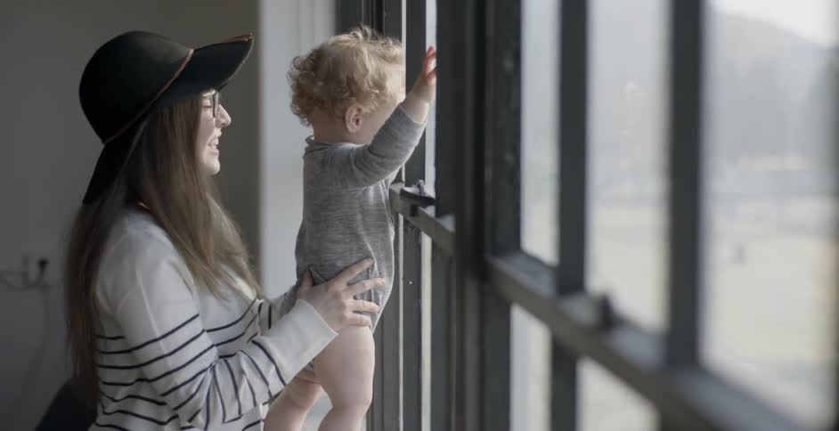 A woman is holding a baby as it taps a window