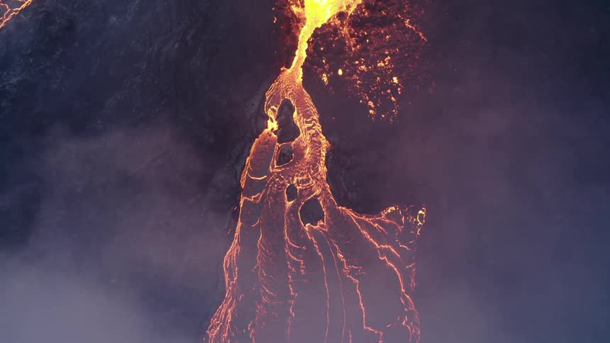 Molten hot lava glows in the darkness as it splashes and flows from an erupting volcano