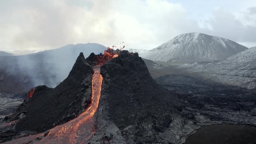 Aerial landscape of a volcano erupting during day time next to a mountainous area