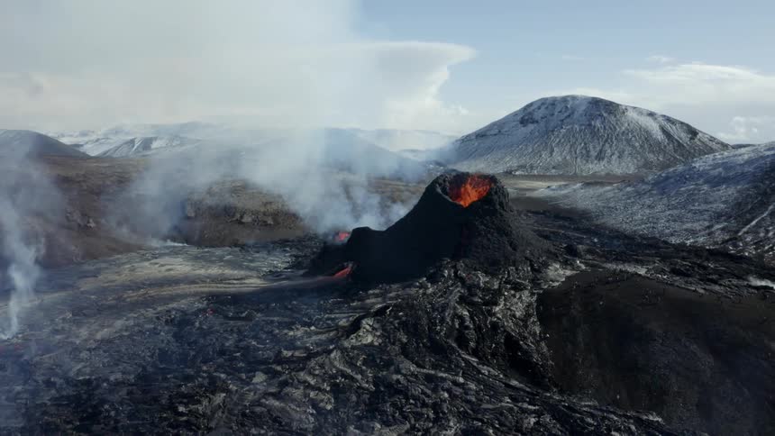 Smoke rises as glowing hot lava from an erupting volcano splashes and flows across the land and a helicopter flies near
