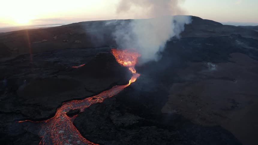 Hot glowing lava splashes and flows as a volcano erupts and smoke rises