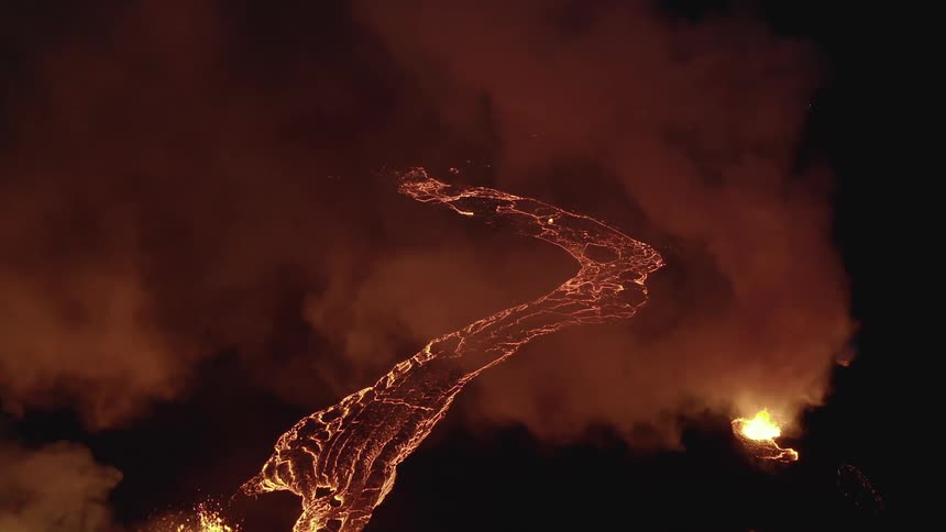 Molten hot lava glows in the darkness as it flows from an erupting volcano