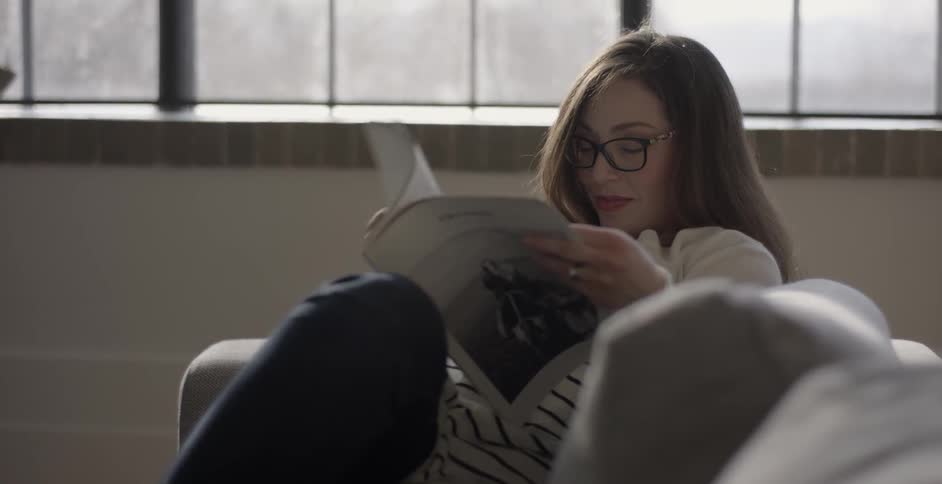A woman is laying on the couch reading a magazine