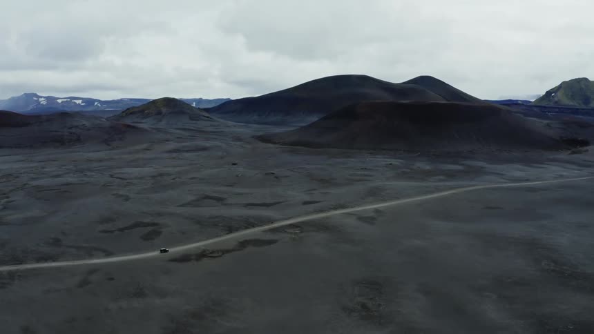 A 4x4 travels on a desert road through barren land and mountains