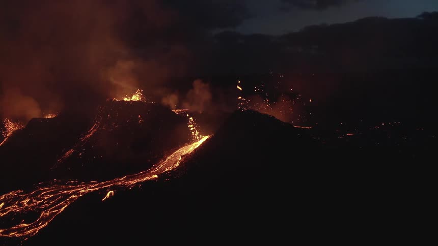 Molten hot lava glows in the darkness as it splashes and flows from an erupting volcano