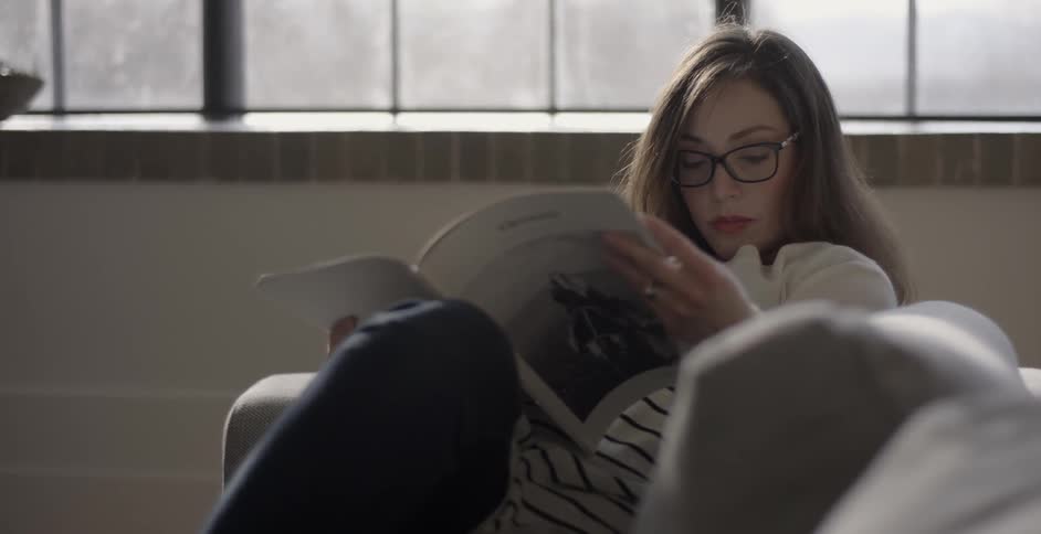 A woman is laying on a couch reading