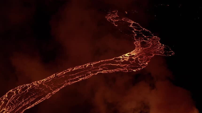 Molten hot lava glows as it flows in the darkness and rising smoke glows red