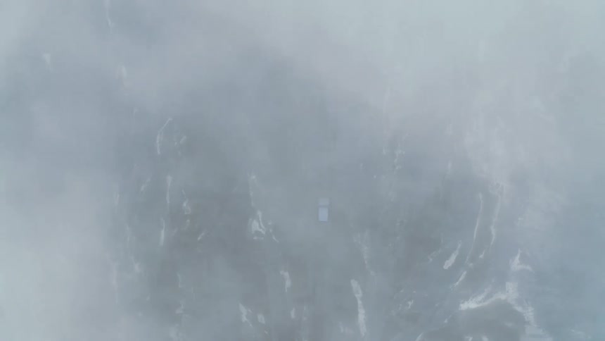 Aerial of vehicle driving through mountainous terrain in winter intermittently obscured by clouds