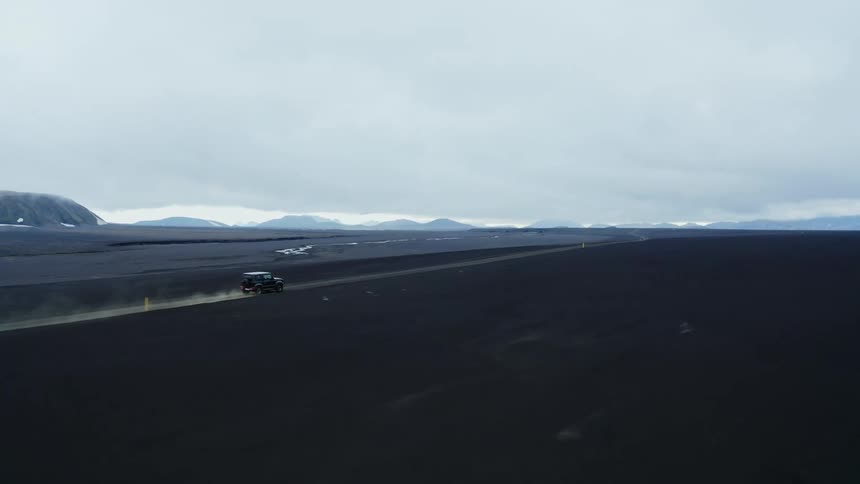 Jeep drives along dirt road through plains near mountains on an overcast day
