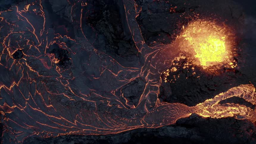 Molten hot lava glows in the darkness as it splashes and flows from an erupting volcano