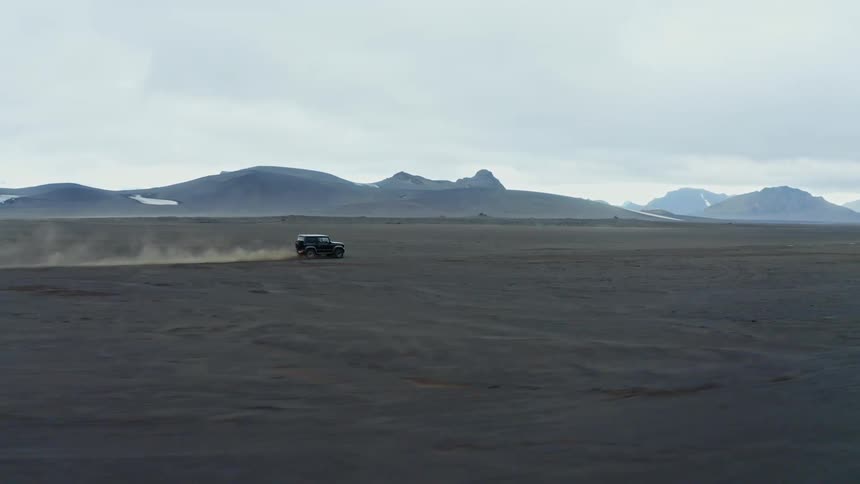 Black jeep drives in the desert with a distant mountain range