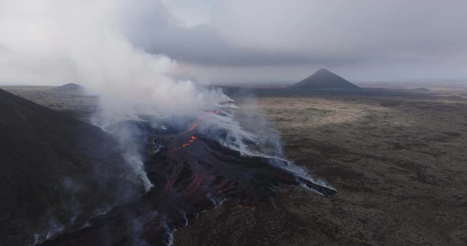 Smoke rises as glowing hot lava from an erupting volcano flows