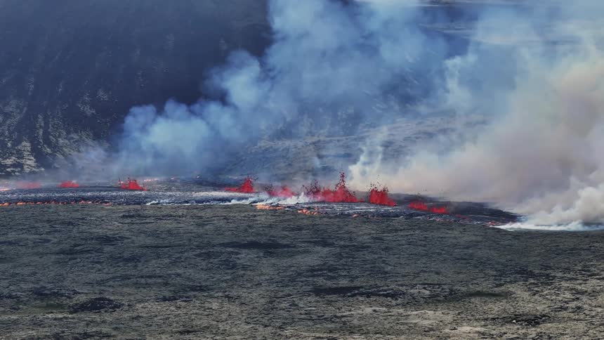 Smoke rises as glowing hot lava from an erupting volcano flows across the land