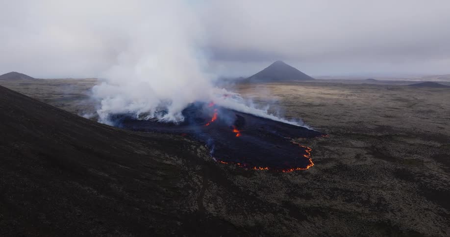 Smoke rises as flaming hot lava from an erupting volcano flows across the land
