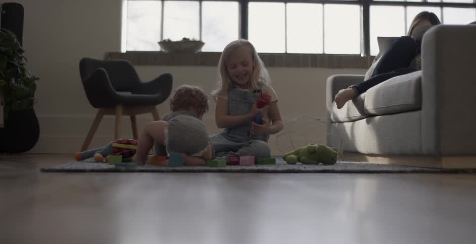 Children play on the carpet as a woman reads on the couch