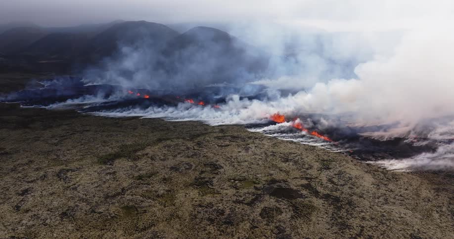 Smoke rises as glowing hot lava from an erupting volcano splashes and flows across the land