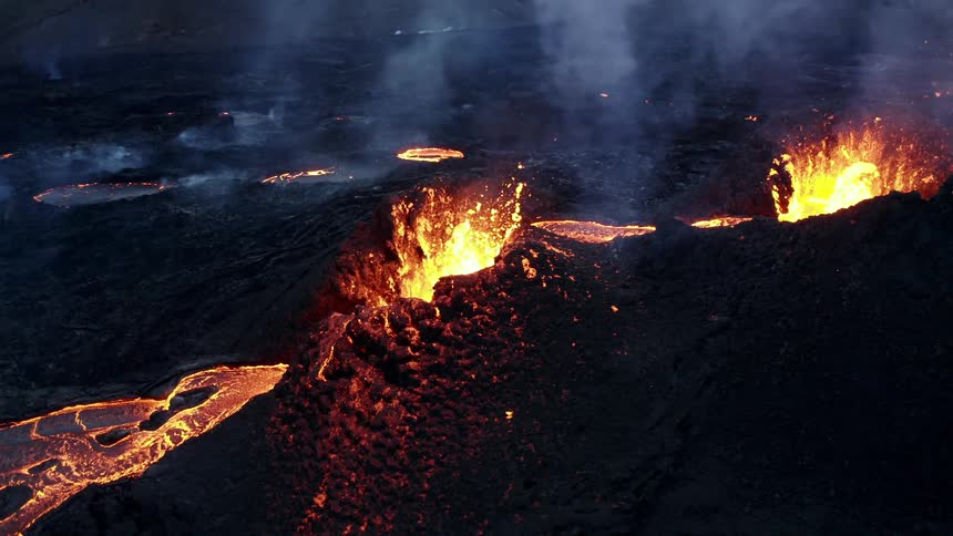 Molten hot lava glows in the darkness as it splashes and flows from an erupting volcano
