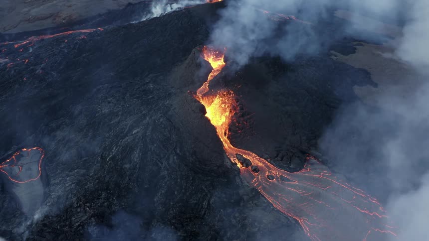 Molten hot lava glows as it splashes from a volcano and flows as smoke rises