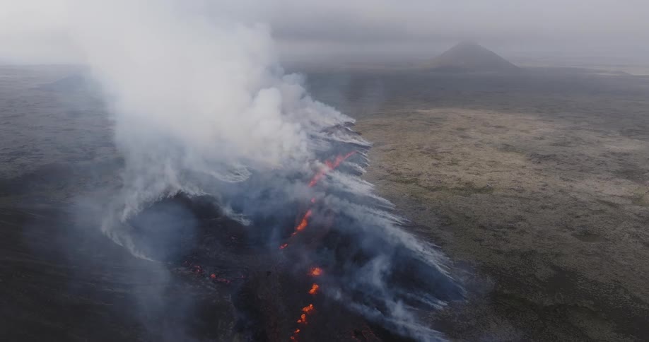 Heavy smoke rises from lava flowing through gully in field on foggy overcast day