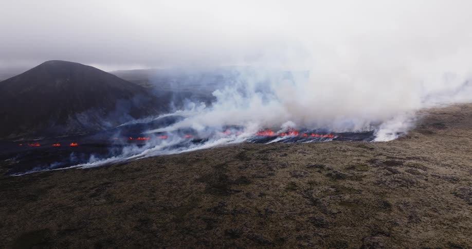 Smoke rises as glowing hot lava from an erupting volcano splashes as it flows across the land