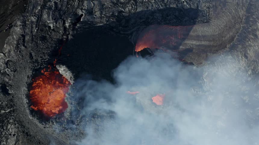 Molten hot lava glows as it splashes from a volcano and smoke rises as lava flows