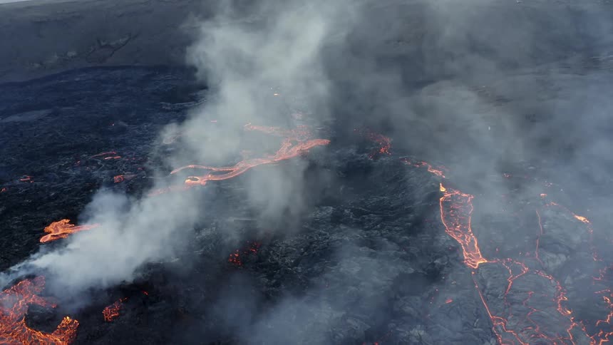 Molten hot lava splashes as it flows from an erupting volcano and smoke fills the air