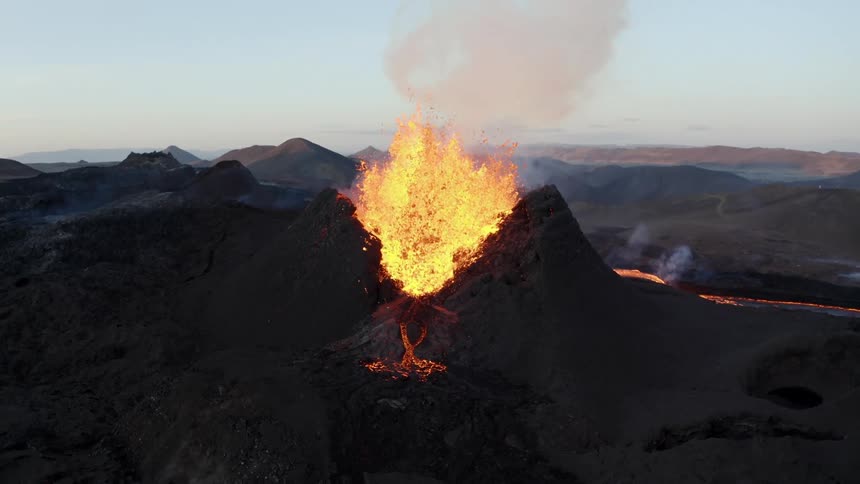 Molten hot lava glows and splashes into the air as it flows from an erupting volcano