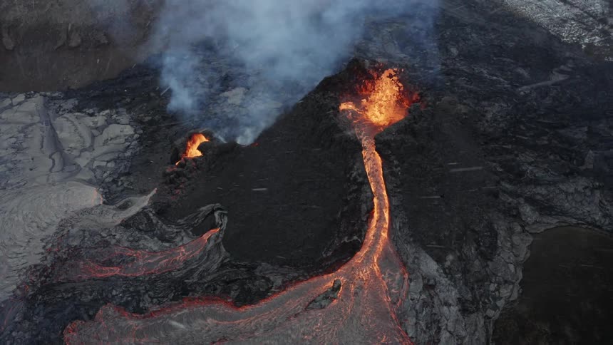 Molten hot lava glows as it splashes from an erupting volcano and smoke rises as lava flows