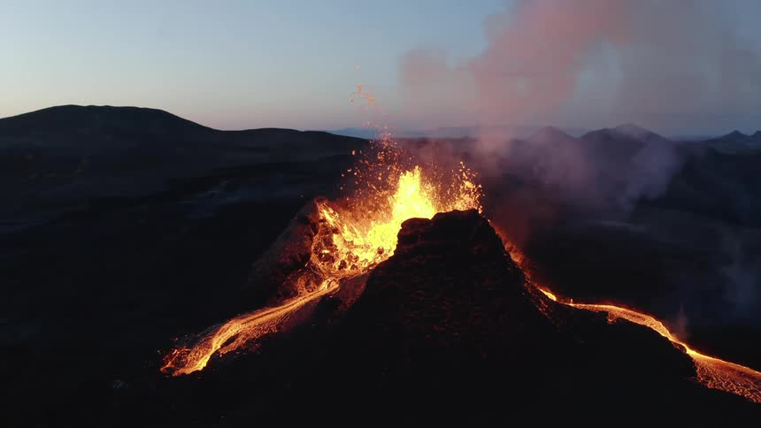 Aerial landscape of volcano erupting next to mountainous area during dusk or dawn