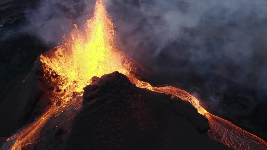 Molten hot lava splashes into the air and flows as a volcano erupts