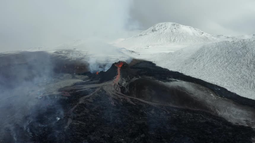 Aerial view of a volcano erupting with lava snowy mountains in the background