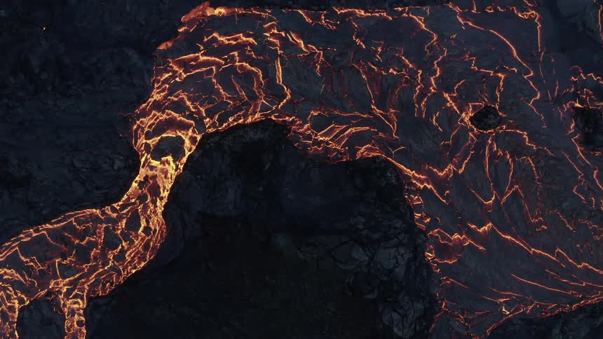 Molten hot lava glows in the darkness as it flows from an erupting volcano