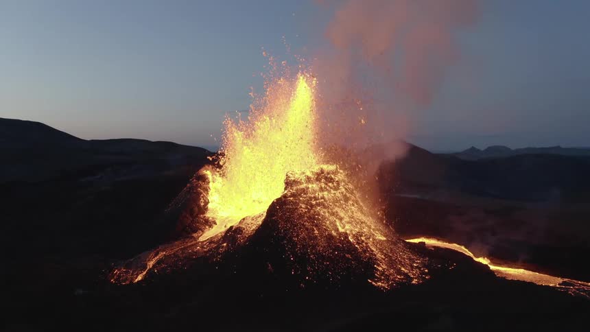 Molten hot lava glows as it splashes high into the air from an erupting volcano