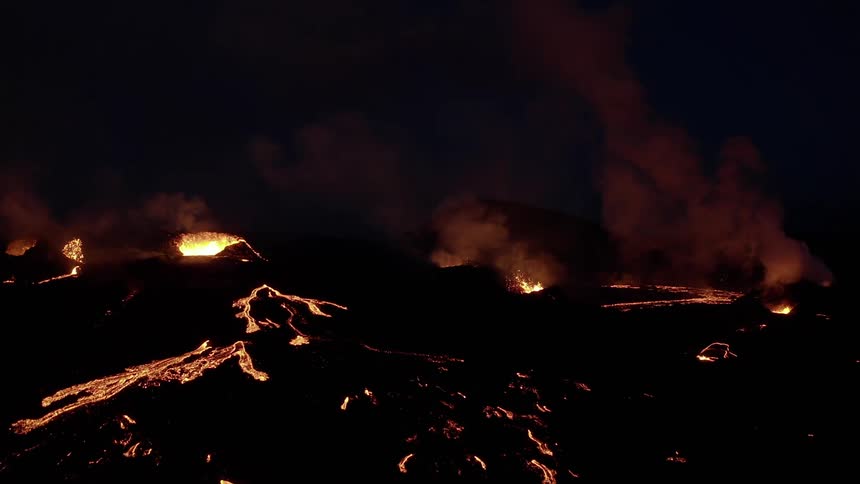Molten hot lava glows in the darkness as it splashes and flows from an erupting volcano