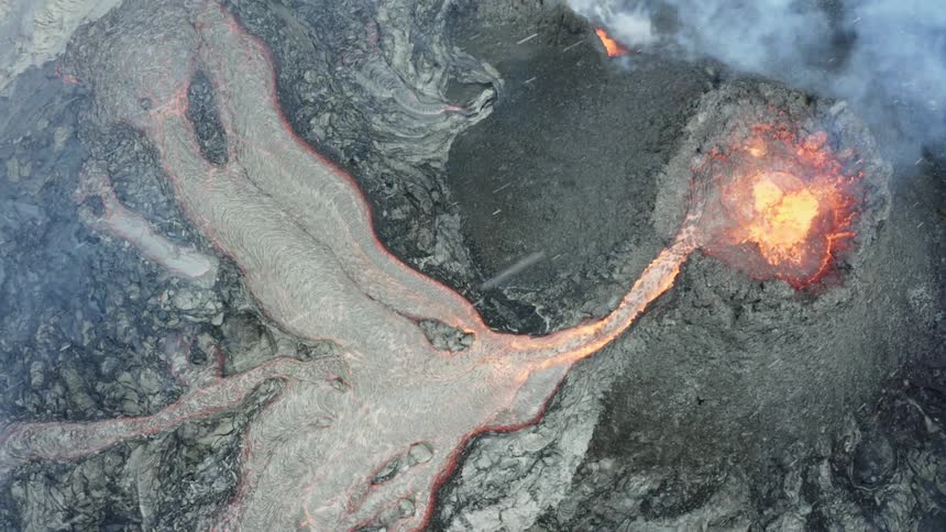 Molten hot lava glows as it splashes and flows from an erupting volcano and snow flies in the air