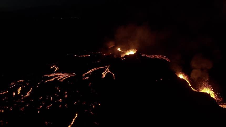Molten hot lava glows in the darkness as it splashes and flows from a volcano